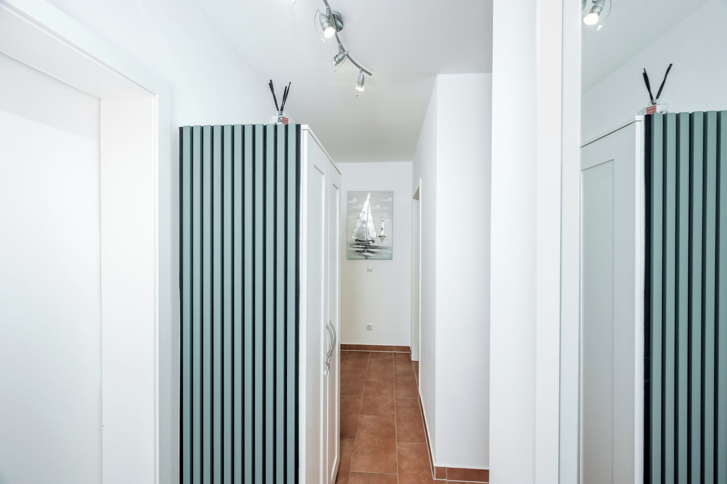 A hallway with vertical blinds, a tiled floor, and a framed picture on the wall.