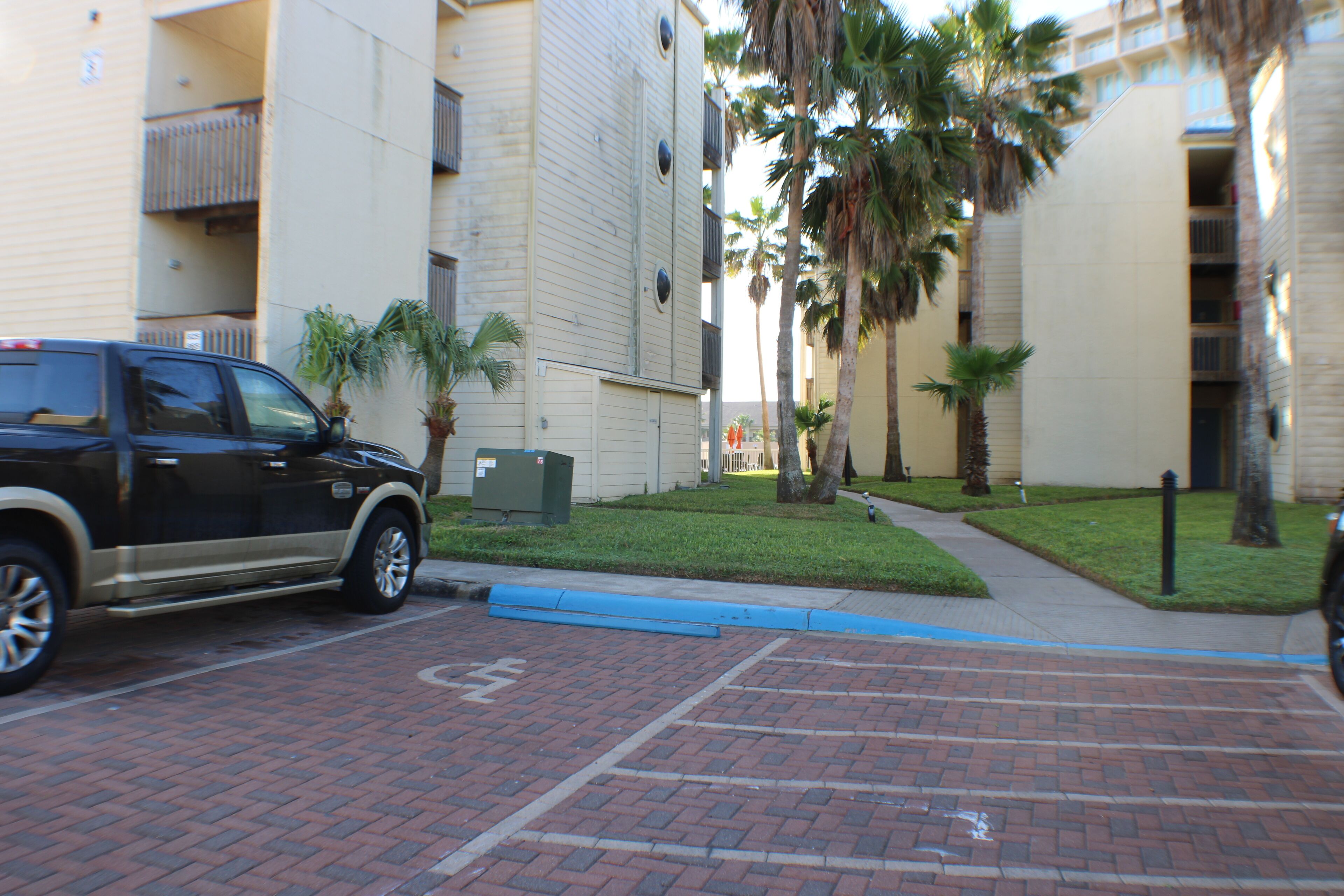 A parking area with a brick pavement, a blue curb, and a black SUV.