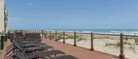 A wooden deck with rows of black lounge chairs facing the beach.