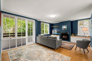 A living room with a grey sofa, a fireplace, and large windows. - Leafy South Yarra Retreat | Charming 3BR w Balcony (South Yarra)