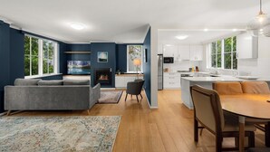 Una cocina moderna con armarios blancos, un comedor con mesa y sillas de madera, un sofá gris y una chimenea.