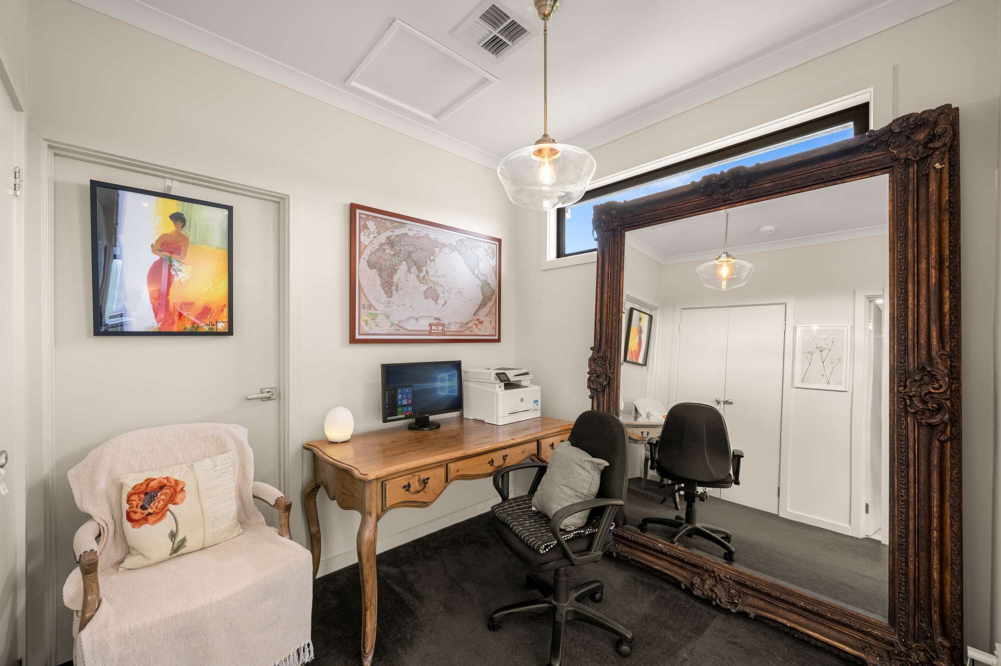 A room with a desk, two chairs, a large mirror, and artwork on the walls.