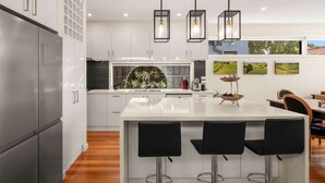 A modern kitchen with white cabinetry, a central island with bar stools, pendant lighting, and artwork on the walls.
