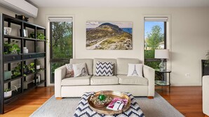 A living room with a sofa, a bookshelf, a painting, and a window with a view.