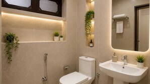 A modern bathroom with a toilet, bidet, and sink. There are potted plants on shelves and a mirror with a towel rack.