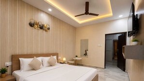 A modern hotel bedroom with a large bed, bedside tables, a ceiling fan, a TV, and a bathroom visible through an open door.