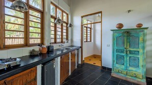 A kitchen with a black countertop, wooden cabinets, a sink, and a teal cabinet with decorative knobs. - Staymaster Ashvini 2BR Villa Jet Pool (Nerul)