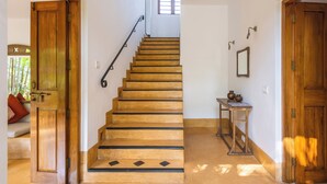 A wooden staircase with a handrail, a small table with a vase, and a mirror on the wall. - Staymaster Ashvini 2BR Villa Jet Pool (Nerul)