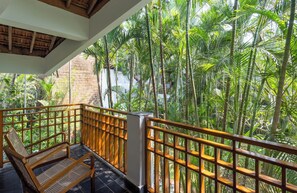 A balcony with a wooden bench, surrounded by a wooden railing, overlooking a lush garden with tall palm trees. - Staymaster Ashvini 2BR Villa Jet Pool (Nerul)