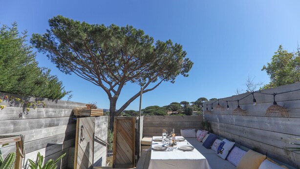 An outdoor dining area with a wooden deck, a table set for two, and a large tree in the background. - STUNNING APARTMENT (Sainte-Maxime)