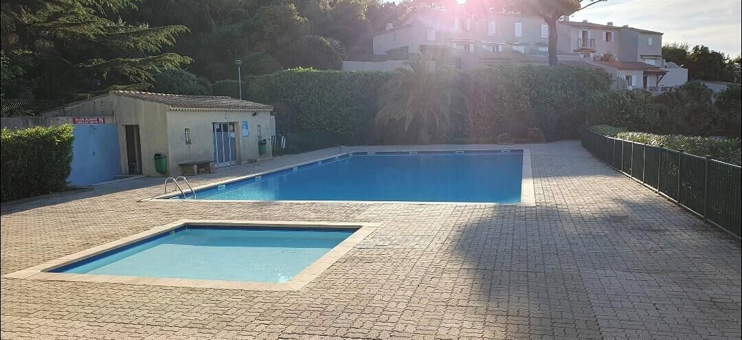 A swimming pool with a tiled deck, a small building with a door, and a fence.