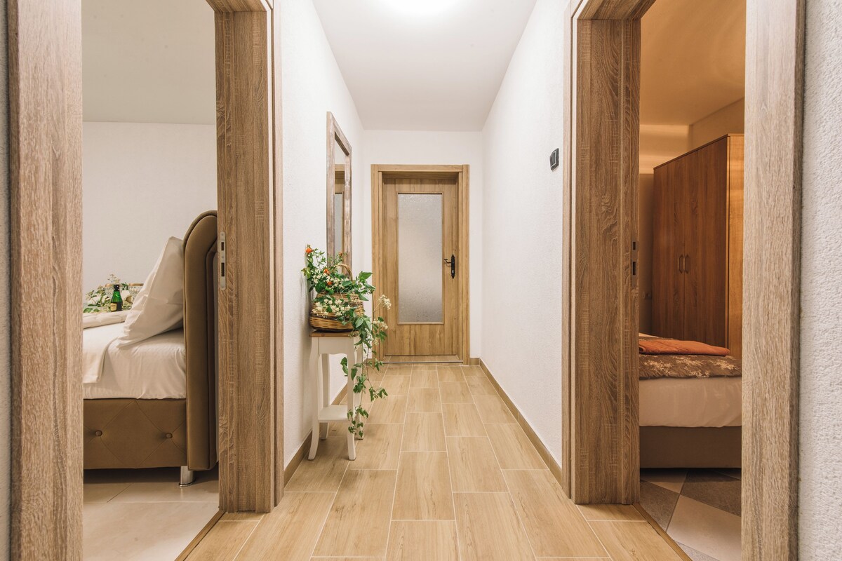 A hallway with a bed, a bedside table with a plant, and a mirror.