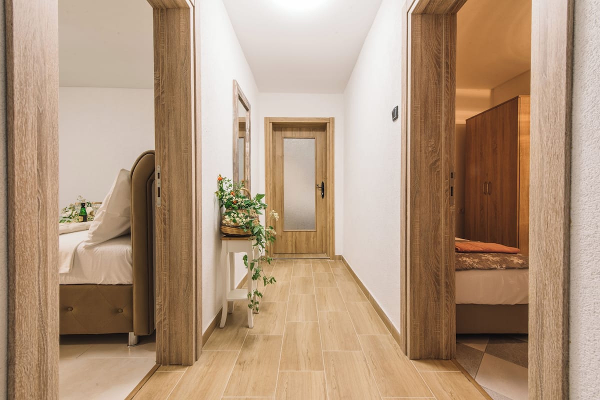 A hallway with a bed, a bedside table with a plant, and a mirror.