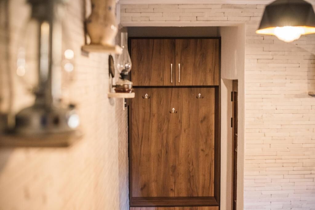 A wooden wardrobe with two doors, a white brick wall, and a hanging light fixture.