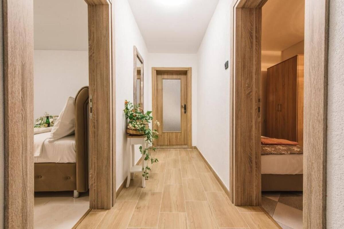 A hallway with a bed, a bedside table with a plant, and a mirror.