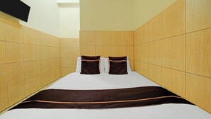 Een enkel bed met een wit-bruine spreidekker, twee kussens en houten paneelwanden.