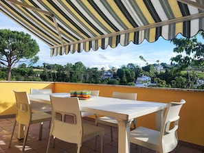 Eine Terrasse mit gestreiftem Sonnensegel, einem weißen Tisch und Stühlen.