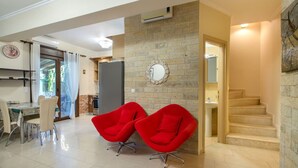 Un espacio moderno con zona de estar, una mesa de comedor, dos sillas rojas, una pared de piedra y una escalera.