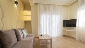 A living room with a sofa, a coffee table, a TV, and a staircase. - Happy Ellen Seafront 1 by Travel Pro Services (Nea Plagia)