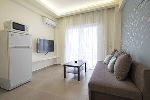 Ein Wohnzimmer mit Sofa, Fernseher, kleinem Tisch, Kühlschrank und Klimaanlage.