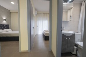 Ein Hotelzimmer mit Bett, einem Badezimmer inklusive Waschbecken und Toilette, sowie einem Flur, der zu einem weiteren Zimmer führt.