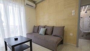 A modern living room with a sofa, a small table, and a window with sheer curtains. - Happy Ellen Seafront 4 by Travel Pro Services (Nea Plagia)