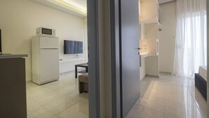 A modern hotel room with a kitchenette, a flat-screen TV, a dining area, and a bathroom with a shower and toilet. - Happy Ellen Seafront 4 by Travel Pro Services (Nea Plagia)