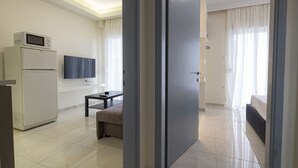 A modern hotel room with a kitchenette, a flat-screen TV, a bed, and a large window with curtains. - Happy Ellen Seafront 4 by Travel Pro Services (Nea Plagia)