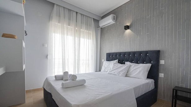 Una moderna camera d'albergo con un letto grande, lenzuola bianche, una testiera scura e un condizionatore d'aria a parete.