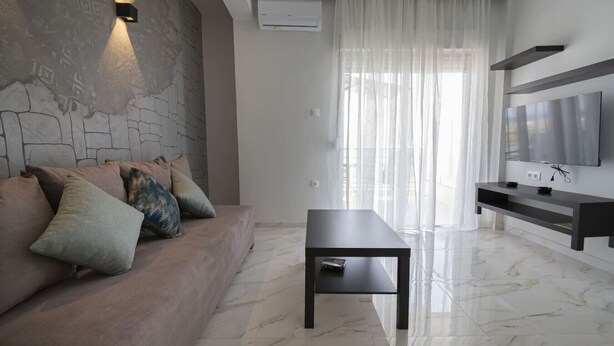 Un salon moderne avec un mur d’accent en pierre, un canapé avec des coussins, une table basse, un téléviseur et une fenêtre ornée de rideaux légers.