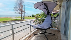 Un balcon avec une chaise et un parasol, une vue sur la route et un arbre.