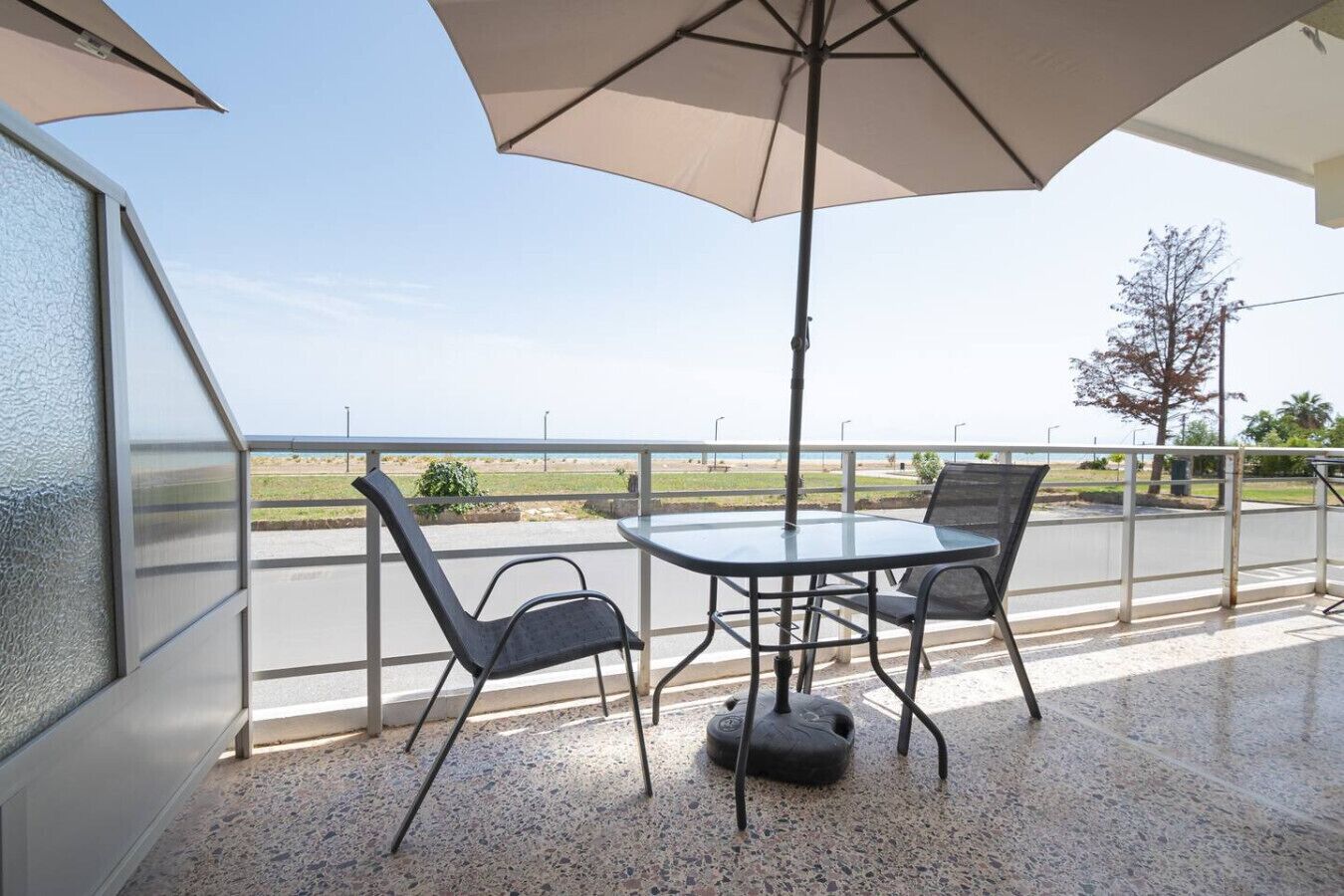 Un balcon doté d’une paroi en verre, de deux chaises, d’une table et d’un grand parasol.