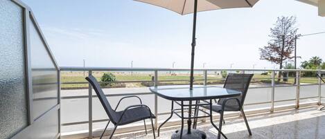 Un balcon doté d’une paroi en verre, de deux chaises, d’une table et d’un grand parasol.