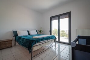 Ein Schlafzimmer mit Bett, Nachttisch, Stuhl, einer Zimmerpflanze und einer Schiebetür zu einem Balkon.