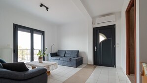 En rummelig opholdsstue med en grå sofa, et lille rundt bord med en plante, og en balkon med gelænder.