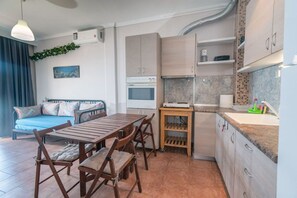 A compact living space with a kitchenette, a dining area, and a sofa. - Seagull House by RentalsPro - Nea Potidaia (Nea Potidaia)