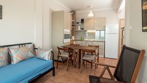 Ett kompakt bostadsutrymme med ett litet kök, en matplats med bord och stolar samt en soffa med mönstrade kuddar.