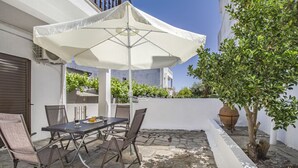 Une terrasse avec une table et des chaises, un parasol blanc et une plante en pot.