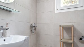 Une salle de bain équipée d’un lavabo, d’un miroir, d’une douche et d’une fenêtre donnant sur la forêt.