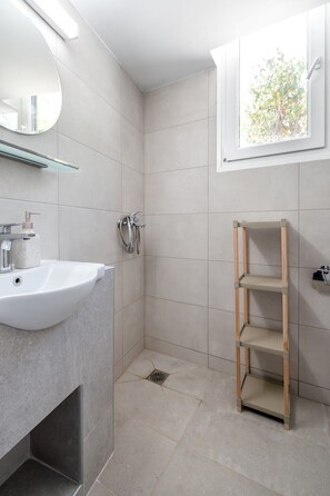 A bathroom with a sink, mirror, shower, and a window with a view of trees. - Filia Apartment Aposperitis by RentalsPro (Nea Fokea)
