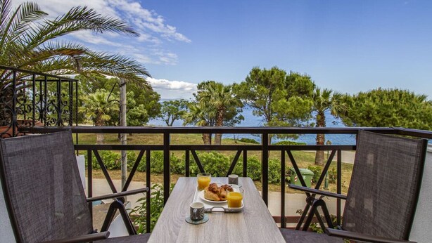 En balkong med ett bord dukat för frukost, med utsikt över en sjö eller ett annat vattendrag och grönområden.