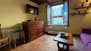 A cozy room with a wooden table, a bench, a dresser, a radiator, and a window with a view of buildings. - Lovely apartment for 3 people with WIFI, A/C, terrace, pets allowed and panoramic view (Cortona)