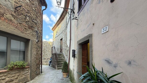 A narrow stone-paved alleyway between buildings with a number '32' sign, a wooden door, and a potted plant. - Lovely apartment for 3 people with WIFI, A/C, terrace, pets allowed and panoramic view (Cortona)