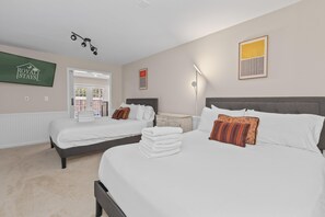 A hotel room with two beds, a flat-screen TV, a bedside table, a lamp, and a door leading to a balcony. - The Blue Angel-In Ground Pool (Charleston)