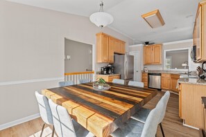 Una cocina moderna con armarios de madera, un refrigerador de acero inoxidable y una zona de comedor con mesa y sillas de madera.