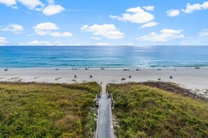 A beach with a wooden boardwalk leading to the shore, surrounded by grassy areas and a clear sky. - NEW Sunrise Beach 510! FREE Beach Service, Heated Pool, FREE Golf & Perks! (Panama City Beach)