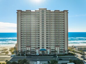 A high-rise hotel with multiple balconies, a beach view, and a parking area. - NEW Sunrise Beach 510! FREE Beach Service, Heated Pool, FREE Golf & Perks! (Panama City Beach)