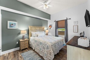 Un dormitorio con cama, mesita de noche, lámpara y vistas al exterior.
