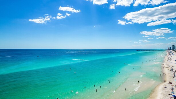 A beach with clear turquoise waters, a pier, and a city skyline in the background. - NEW Sunrise Beach 510! FREE Beach Service, Heated Pool, FREE Golf & Perks! (Panama City Beach)