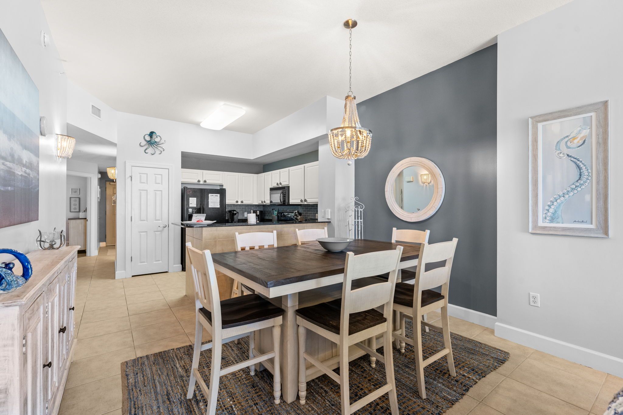 A modern kitchen with white cabinets, a dark wooden dining table, and a chandelier.
